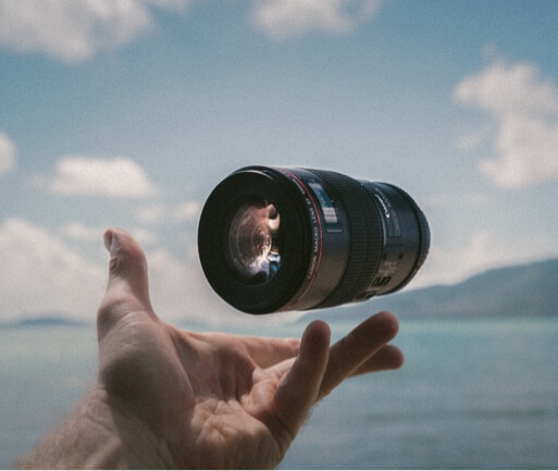 A camera lens suspended above someone's hand with a lake and blue sky as the background